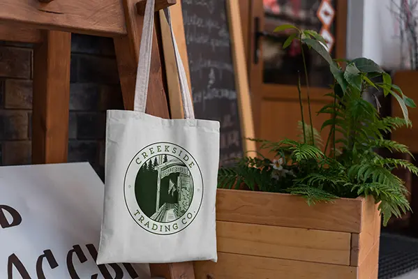 The Creekside Trading Co. logo printed on a canvas tote hanging outside a storefront.