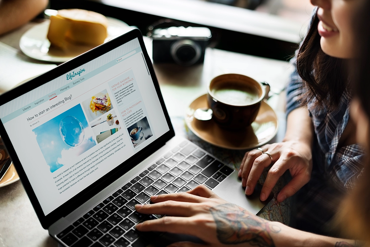 Person browsing a blog on a laptop while sitting in a café with a coffee cup nearby.