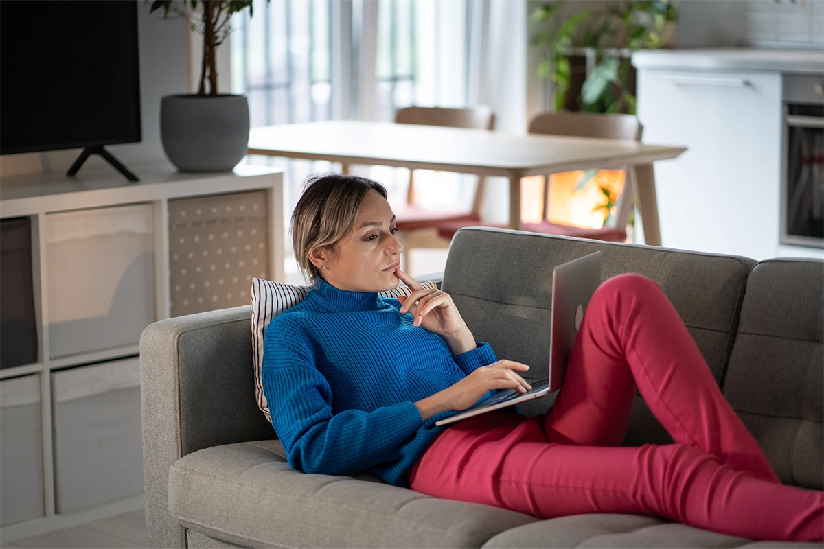 Focused Woman - Bold Marketing & Design Woman in a blue sweater sitting on a couch using a laptop and working from home.