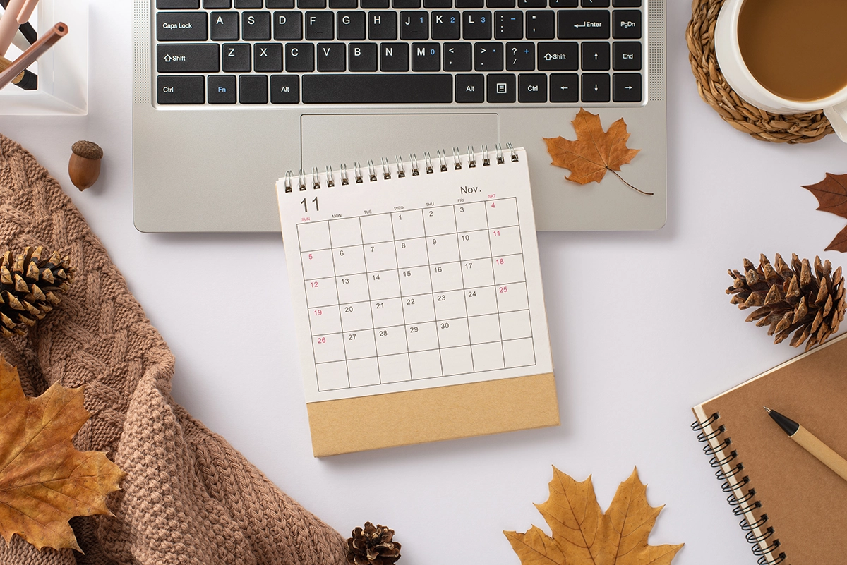 Autumn-themed flat lay with laptop, calendar, coffee, pinecones, and brown sweater symbolizing fall productivity