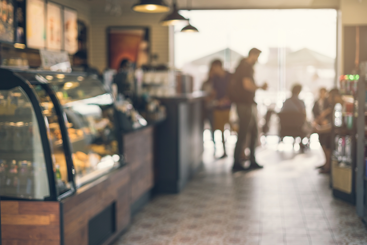 Blurred interior of a coffee shop with a pastry display, customers in the background, and warm natural lighting creating a casual atmosphere.