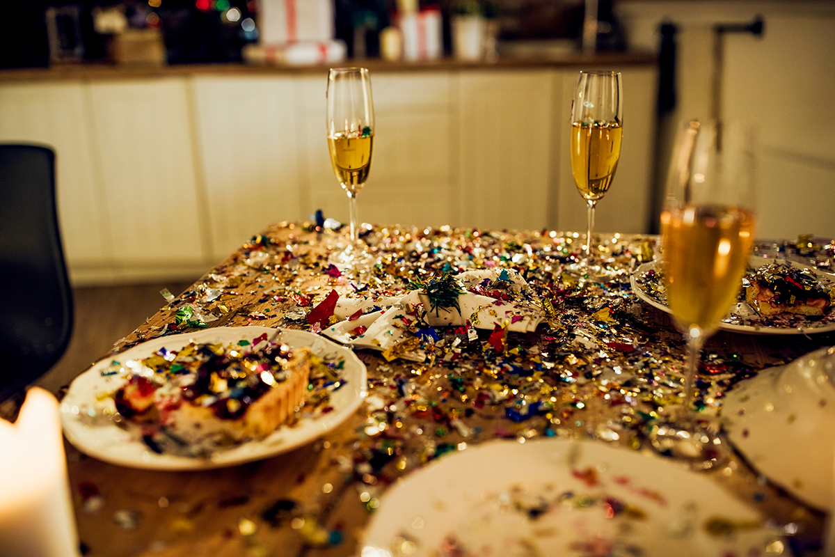 Dining table covered in confetti with partially eaten desserts and champagne glasses, suggesting a celebration after a New Year gathering.