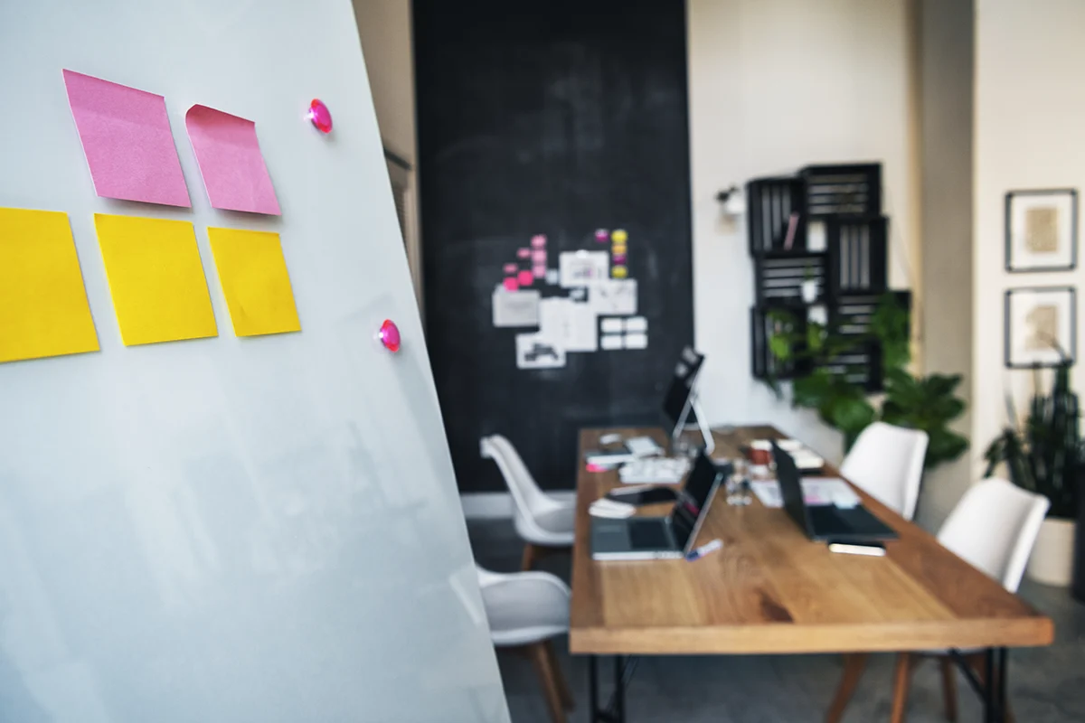 Modern office conference room with a planning board displaying colorful sticky notes, laptops on a wooden table, and a collaborative workspace setting.