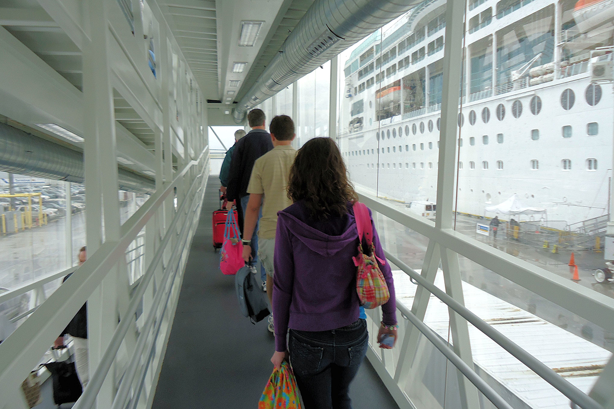 Travelers walking through a terminal boarding a large cruise ship with luggage