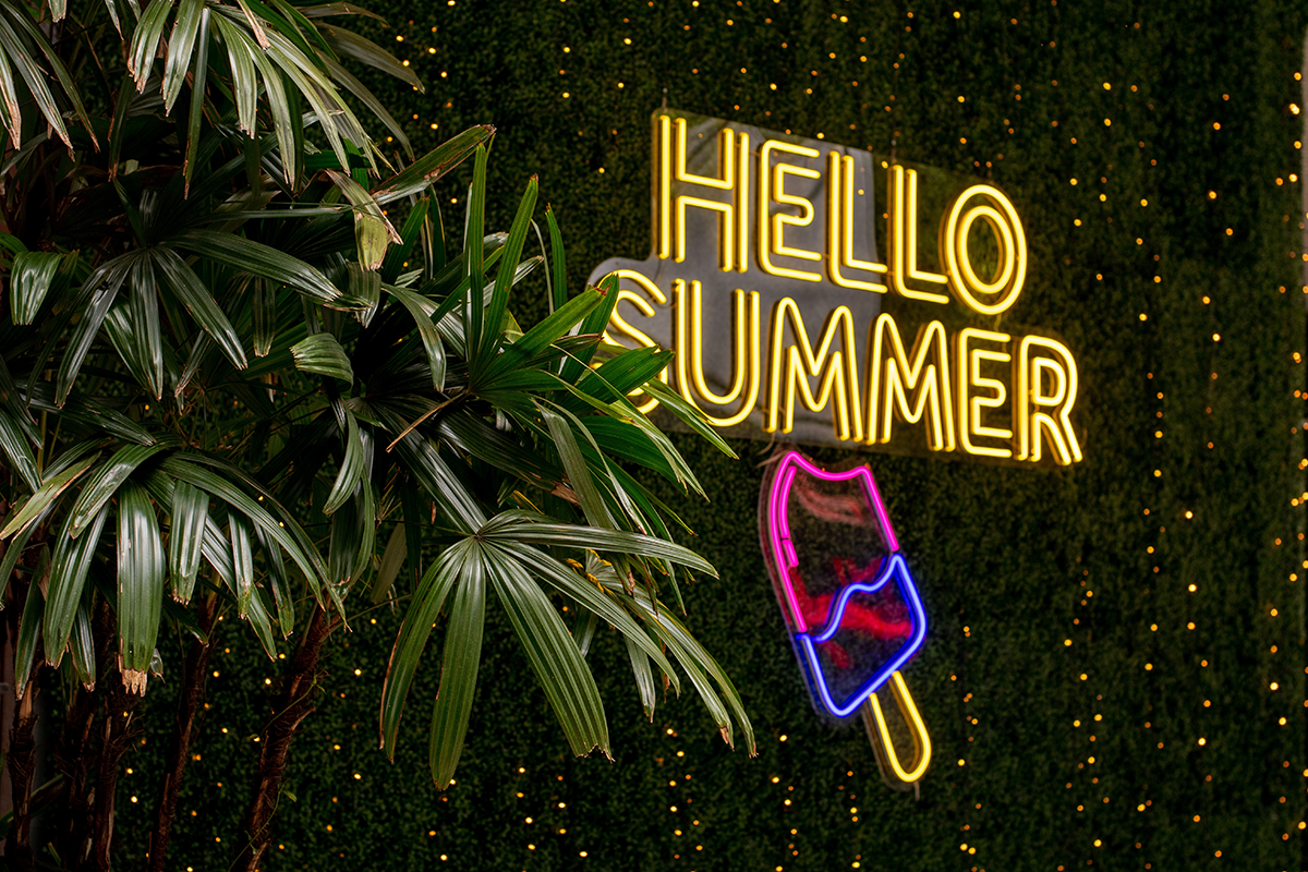Neon “Hello Summer” sign with tropical plants and ice cream graphic for seasonal marketing
