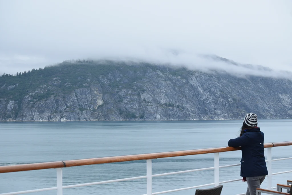 Woman standing on cruise ship deck overlooking misty Alaska coastline and mountains