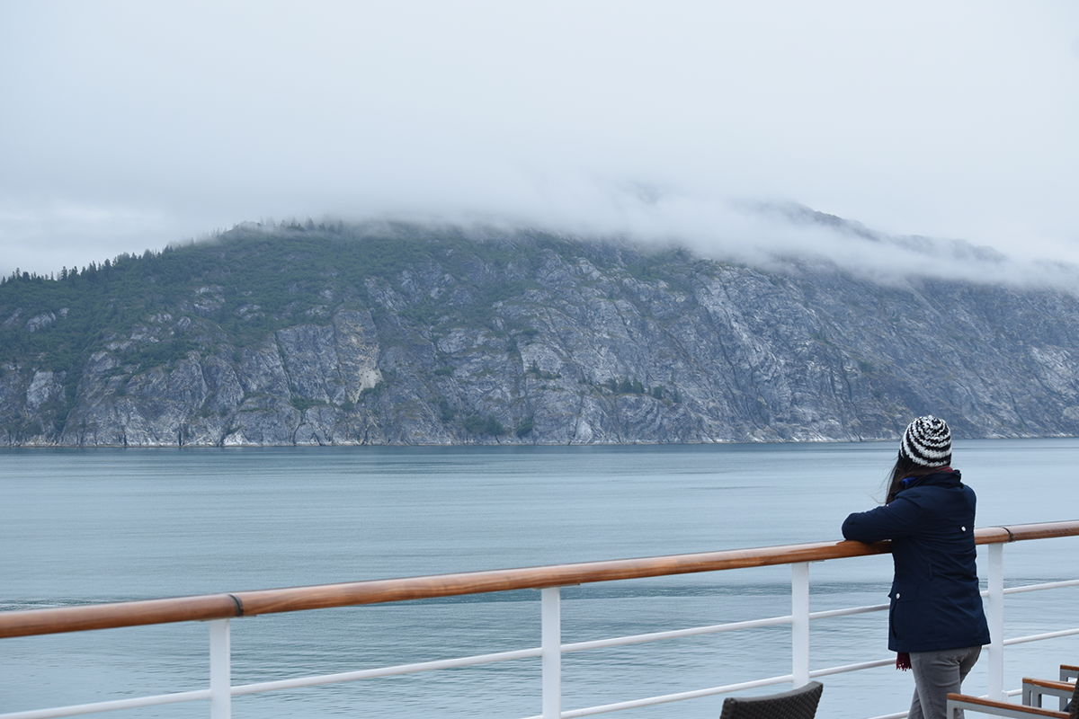 Woman standing on cruise ship deck overlooking misty Alaska coastline and mountains