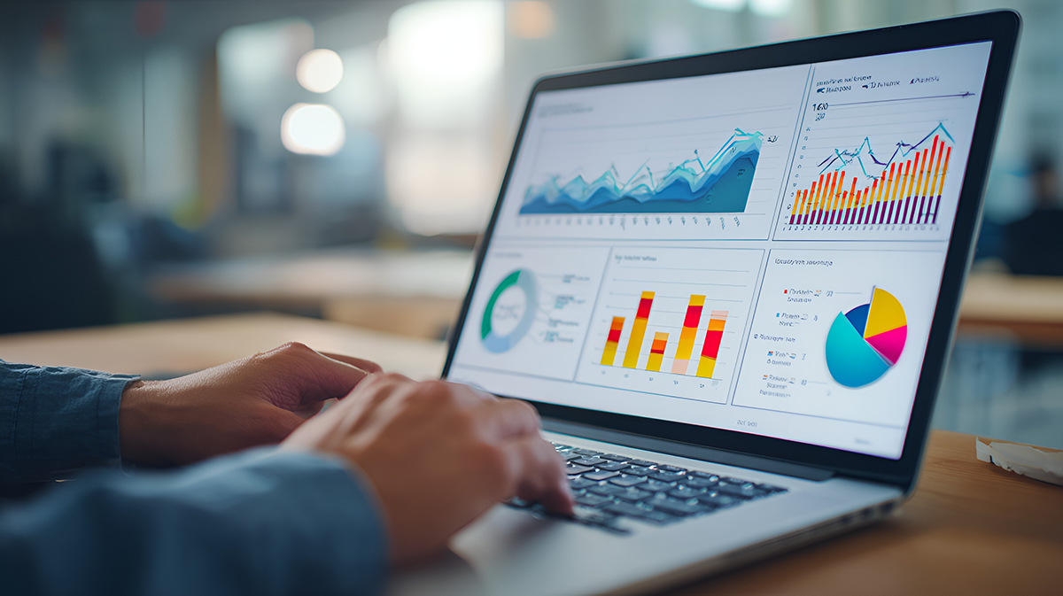 A person uses a laptop displaying colorful web analytics dashboards with charts, graphs, and a pie chart.