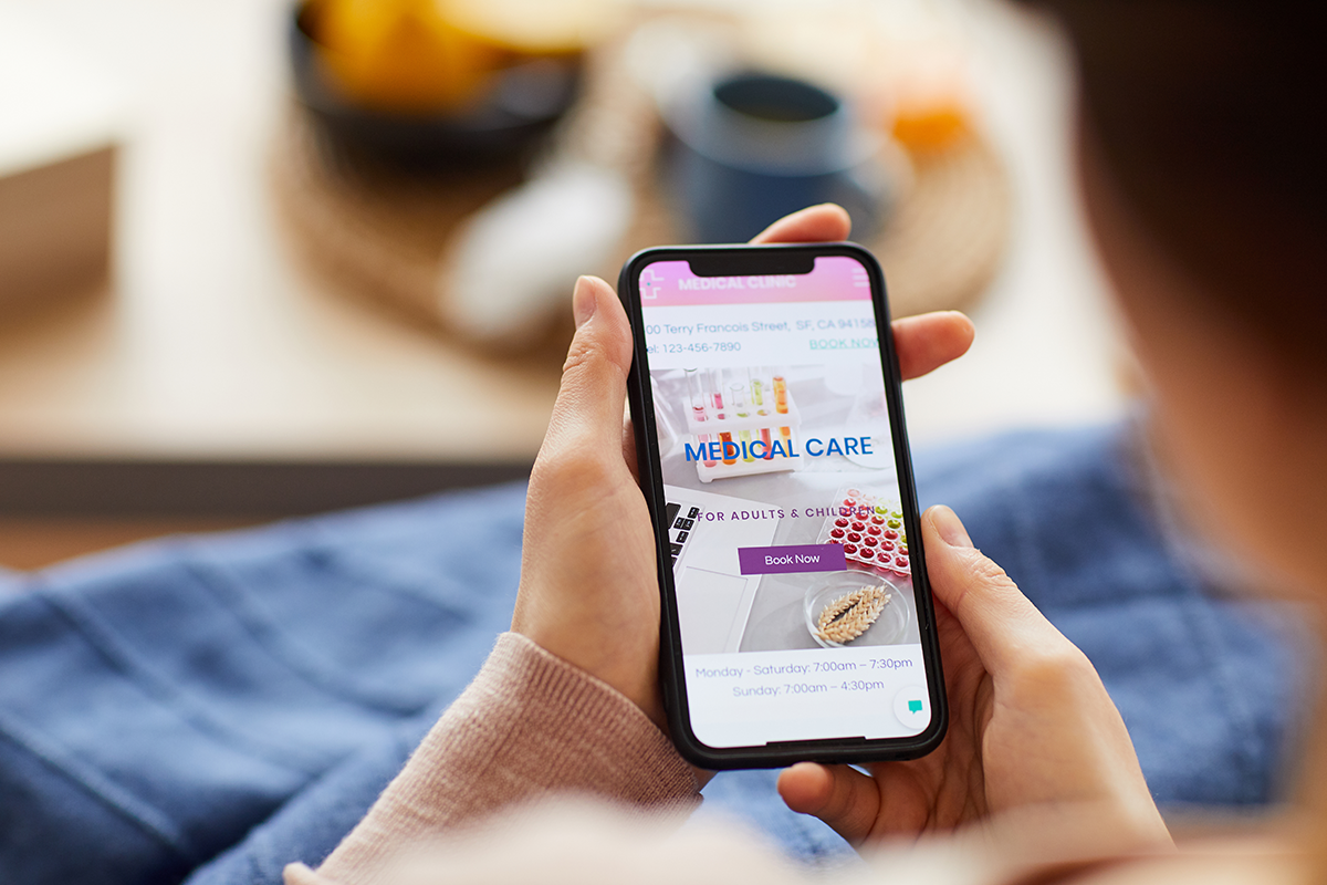 Person holding a smartphone displaying a medical clinic website with a prominent “Book Now” button.