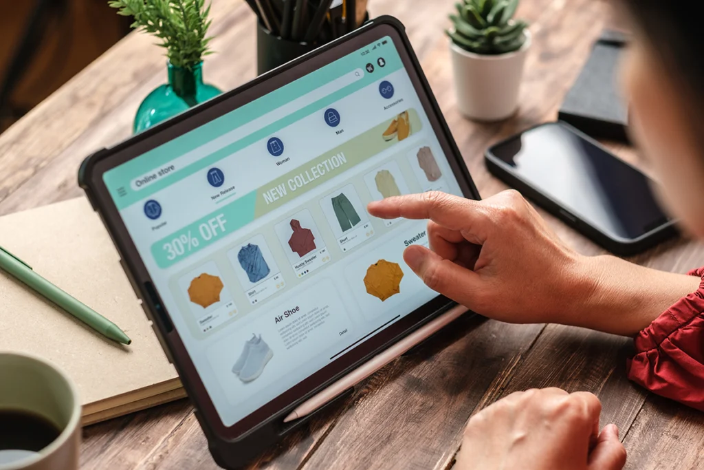Person browsing an online clothing store on a tablet, pointing at products displayed on the screen.